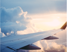 A photo of the right wing of an airplane flying among clouds, sun dawning in the background